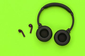 Wireless large stereo headphones and small earbuds on green background. Top view