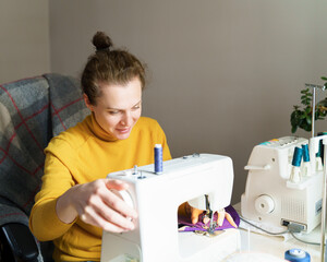 Creative hobby for moms. Side view of woman seamstress dressmaker in casual clothes using sewing machine to sew cloth while working remotely at home, sitting at creative workspace and making clothing