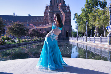 Wall Mural - Middle-aged Hispanic woman in turquoise dress with rhinestones, doing belly dance figures. Belly dance concept.