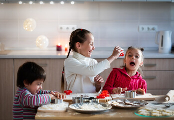 Wall Mural - Three children preparing cookies for celebration and having fun at home