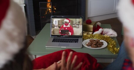 Sticker - Rear view of caucasian couple wearing santa hats having a videocall on laptop during christmas