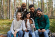 © Seventyfour - Diverse group of friends enjoying hike in forest and looking at camera while sitting on log, copy space