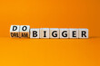 Dream and do bigger symbol. Turned wooden cubes and changed words dream bigger to do bigger. Business and dream and do bigger concept. Beautiful orange background, copy space.
