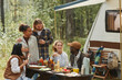 © Seventyfour - Diverse group of young people enjoying picnic outdoors while camping with trailer van