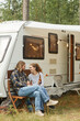 © Seventyfour - Vertical full length shot of young couple enjoying picnic outdoors while camping with camper van, copy space