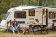 © Seventyfour - Wide angle view of friends enjoying outdoors while camping with van in forest, copy space