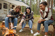 © Seventyfour - Group of young people roasting marshmallows while enjoying camping with friends in forest, copy space