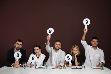 Wall Mural - Panel of judges holding different score signs at table on brown background