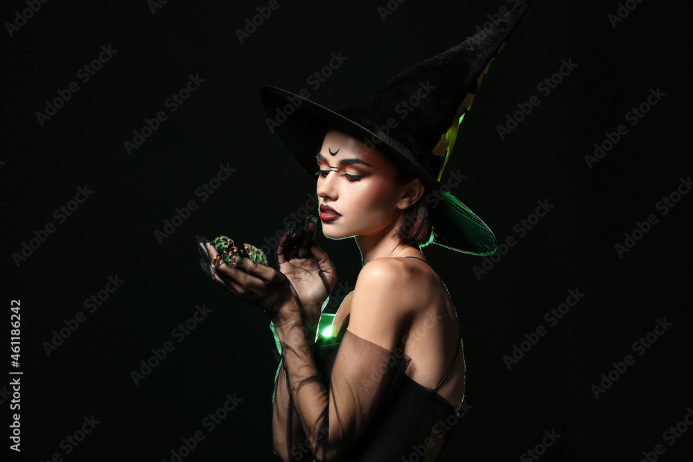 Young witch with spider on dark background