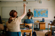 © Maskot - Teenage student raising hand while studying in high school classroom