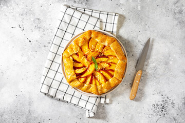 Wall Mural - French galette or pie with peaches and in a white plate on a light gray culinary background top view. Summer homemade sweet pastries