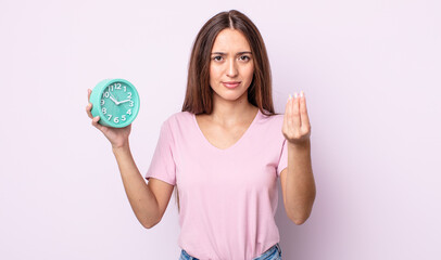 Poster - young pretty woman making capice or money gesture, telling you to pay. alarm clock concept