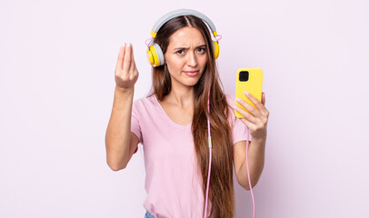 Poster - young pretty woman making capice or money gesture, telling you to pay. headphones and smartphone