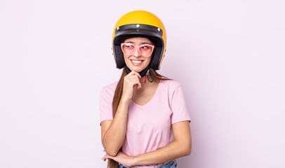 Poster - young pretty woman smiling with a happy, confident expression with hand on chin. motorbike rider and helmet