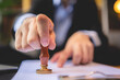 © chokniti - Close-up of a person's hand stamping with approved stamp on approval certificate document public paper at desk, notary or business people work from home, isolated for coronavirus COVID-19 protection