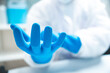 © chokniti - Closeup of hands of a young unrecognizable scientist, researcher and doctor wearing blue hand gloves with white PPE kit and uniform with covid-19 face protection mask for safety in laboratory