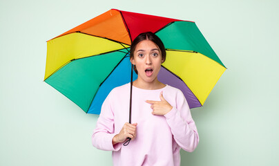 Poster - young pretty woman looking shocked and surprised with mouth wide open, pointing to self. umbrella concept