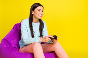 Wall Mural - Portrait of attractive cheerful girl sitting in chair playing game spending free time isolated over bright yellow color background