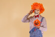 © Ezequiel Martínez - Payaso diabólico, llamando por teléfono móvil, con la calabaza de Halloween, en fondo marrón con espacio para texto.