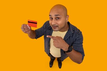 Wall Mural - Portrait of a bald man pointing towards the credit card in hand against plain background.