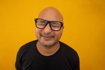 Wall Mural - Portrait of a bald man wearing eyeglasses smiling against plain background with closed eyes.