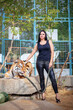 A beautiful girl in black clothes with black hair holds a tiger on a leash