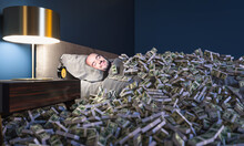 Smiling Man Sleeping In A Bed Covered With Dollars