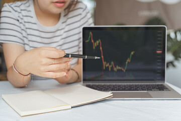 Wall Mural - Young adult Asian trader, investor, businesswoman pointing on computer laptop with graph chart. Woman online teaching in business money investing, stock market, Bitcoin Cryptocurrency trading at home.