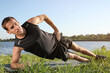 © New Africa - Sporty man doing side plank exercise on green grass near river