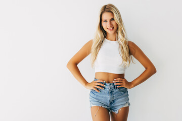 Wall Mural - young blonde girl in short denim shorts and a white t-shirt on white background