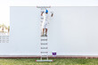 © ADDICTIVE STOCK - Back view of a young painter painting on a ladder