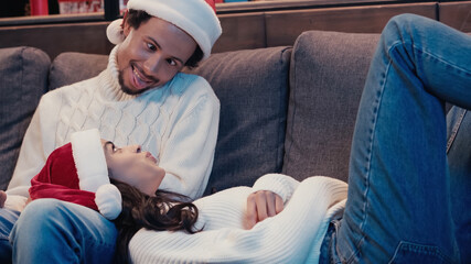 Wall Mural - african american man in santa hat sticking out tongue near woman on cough