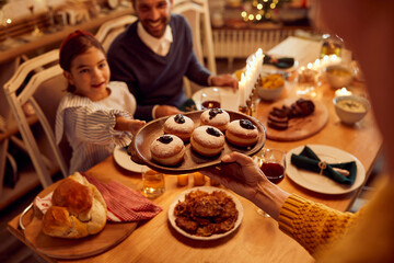 Close-up of mother serves sufganiyah for desert while having family meal on Hanukkah.