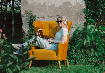 girl sitting in armchair and working on laptop in the garden at home office