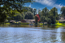 A Gorgeous Shot Of The Vast Still Blue Lake Water With Lake Front Homes Surrounded By Lush Green And Autumn Colored Trees With Blue Sky And Clouds At Lake Peachtree In Peachtree City Georgia