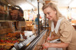 © mad_production - Cheerful mature woman looking at desserts on retail display at bakery store