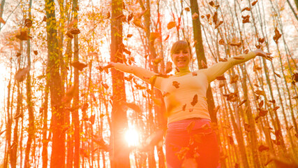 Wall Mural - PORTRAIT: Smiling Caucasian girl plays with dry leaves on a sunny autumn day.