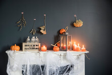 Halloween Home Decoration. Plastic Toy Skeletons In A Wooden Box On A Fireplace Against A Dark Blue Wall. A Garland Of Skeletons. Cobweb On The Dresser. Orange Candles And Lantern.