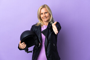 Wall Mural - Middle age woman holding a motorcycle helmet isolated on purple background shaking hands for closing a good deal