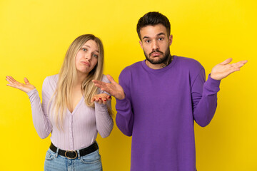 Wall Mural - Young couple over isolated yellow background having doubts and with confuse face expression