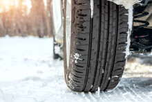 Close-up detail view of car wheel with unsafe summer tread tire during driving through slippery snow road at winter season. Danger traffic accident collision risk. Seasonal tyre switch concept