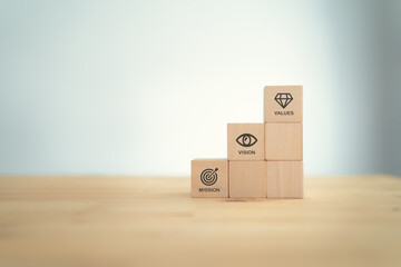 Mission vision values concept icon on wooden cubes stairs on beautiful grey background. Copy space. Used for banner to communicate organization to identify business policy and direction.