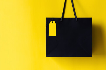 Black shopping bag with blank yellow price tag with yellow background for Black Friday shopping sale concept.