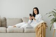 © Serhii - Portrait of a cheerful young woman using mobile phone while relaxing on a couch at home