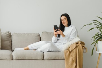 portrait of a cheerful young woman using mobile phone while relaxing on a couch at home