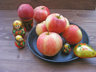 Composition of red and yellow apples on black cast iron plate with traditional russian nesting dolls matrioshka and painted spoon on brown wooden table