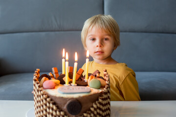 Poster - Cute child, boy, celebrating his birthday at home with colorful cake