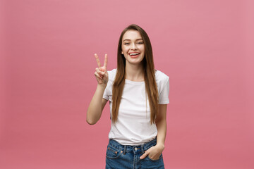 Portrait of a cheerful trendy woman showing two fingers sign over pink background