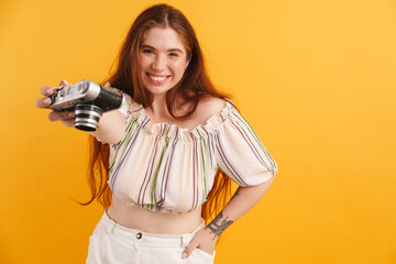 Wall Mural - Young ginger woman reaching retro camera and smiling