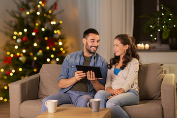 Sticker - technology, winter holidays and people concept - happy couple using tablet computer at home in evening over christmas tree lights on background